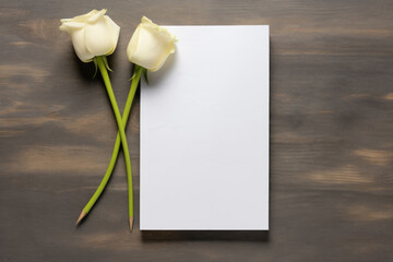 Mockup two white roses beside a blank white paper sheet on a dark wooden background.Greeting card or invitations for of Valentines day or birthday. Womens day and mothers day.Copy space for text.