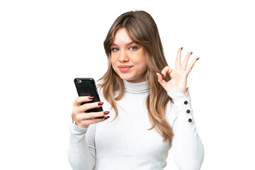 Fototapeta premium Young girl over isolated chroma key background using mobile phone and doing OK sign