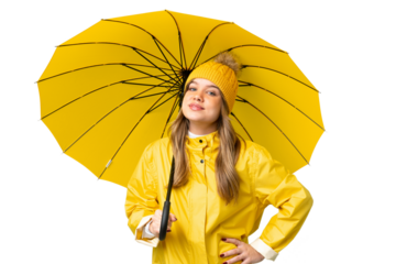 Young girl with rainproof coat and umbrella over isolated chroma key background posing with arms at hip and smiling