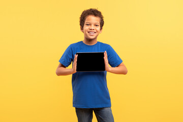 Happy boy in blue shirt holding tablet with blank screen on yellow background