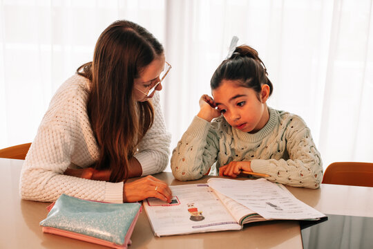Mom helping her daughter with school homework in the kitchen