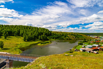 River with suspension bridge at old Urals village, Russia.