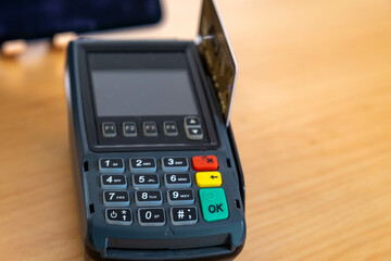 credit card terminal merchant paying confirming a purchase by pressing the green button for sale on the wooden table using credit card in machine slot. Blurry background colourful tablet. out of focus
