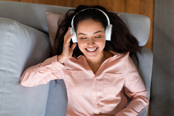 Happy woman in headphones enjoying music while lounging on sofa