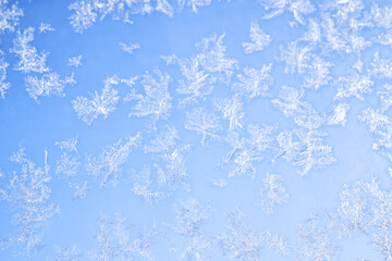Abstract winter background. Frost on a frozen window against the blue sky.