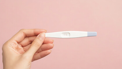 Young woman hand holding pregnancy test on pastel pink background with copy space