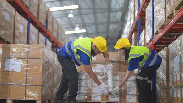 Warehouse workers wrapping plastic seal cover box for packing the items in a large warehouse. man sealing cardboard boxes for shipping in cargo product stock.
