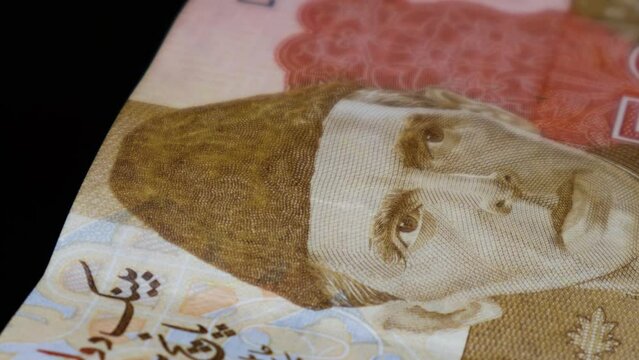 A closeup shot of Pak Rupee 5000 denomination bank note's security feature, including raised ink and 3D security ribbon; while rotating on an automatic display table. 