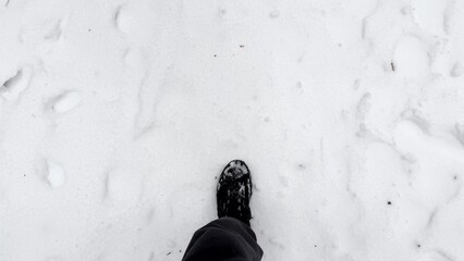 Point of view to male foot stepping on snowy path at winter park. Legs of young man in sneakers...