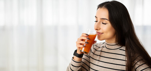 Savoring the moment, a young woman in a striped turtleneck gently enjoys her carrot juice