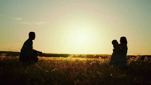 Family enjoys playful moments and sun casts silhouettes over wheat field. Family joyful playing in field of tall wheat. Family at dusk delighted of nature while daughter runs from father to mother hug