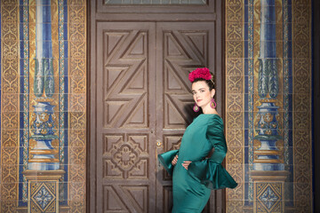 Obraz premium Young, pretty, blonde woman in typical green colored flamenco suit, posing with beautiful tiled wall in background. Flamenco concept, typical Spanish, Seville, Andalusia.