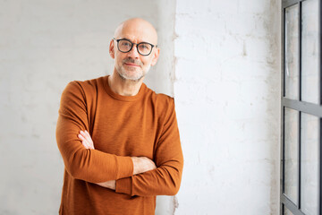 Portrait of mid aged man wearing casual clothes and standing with arms crossed at white wall - obrazy, fototapety, plakaty