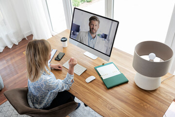 Blond haired woman sitting at home and using computer for video call