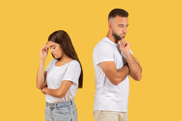 Concerned young couple in white t-shirts standing back to back with worried expressions