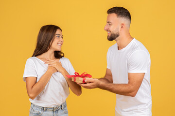A joyous young woman looks at a smiling man who is giving her a small gift box