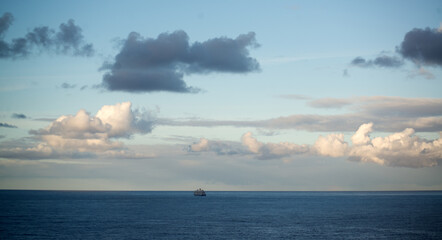 Blue sea with a cruise ship going into the distance and clouds in the sky - 709256340
