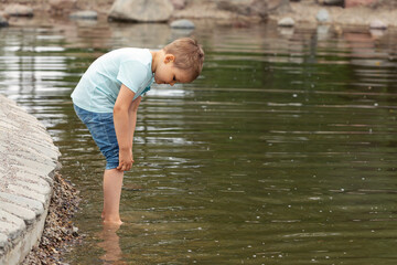 A little boy raises his jeans so that he can wade into the water and not get wet