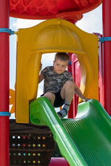 A portrait of a 6-year-old boy is framed in a colorful plastic slide on a children's playground