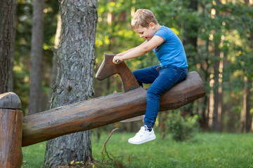 Cheerful emotional little boy swings on a balance beam in the forest background