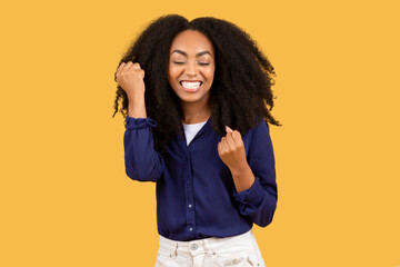 Portrait of joyful african american lady celebrating success, shaking fists and exclaiming with...
