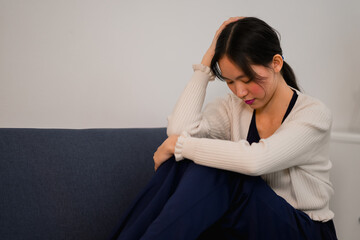 Obraz premium Depressed young woman sitting on couch in the living room at home, look aside sit on blue sofa.