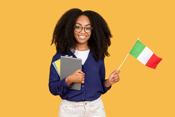 Smiling black lady student with Italian flag, enjoy exchange study, courses, isolated on yellow...
