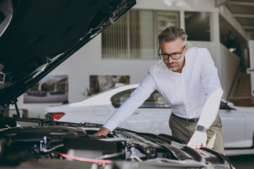 Adult serious man customer male buyer client wearing shirt examining motor open car hood choose...