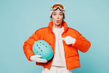 Young fun skier woman wear warm padded windbreaker jacket hat ski goggles mask hold point index finger on helmet travel rest spend weekend winter season in mountains isolated on plain blue background. © ViDi Studio