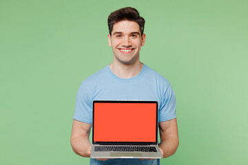Young IT man wearing blue t-shirt white title volunteer hold use work on blank screen laptop pc computer isolated on plain green background. Voluntary free work assistance help charity grace concept.