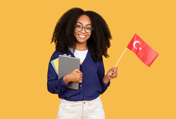 Happy black lady student with backpack and copybooks, holding a Chinese flag, on yellow background