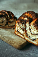A homemade cinnamon roll, cut in half, lies on the kitchen cutting board.