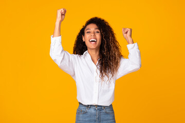Joyful black woman shaking fists raising arms in victory, studio