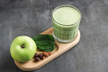Green detox smoothie in a glass, blended vegetarian drink from spinach leaves, apple, banana fruit and nuts on dark background, healthy eating concept