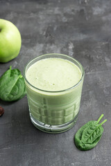 Green detox smoothie in a glass, blended vegetarian drink from spinach leaves and apple fruit on dark background, healthy eating concept