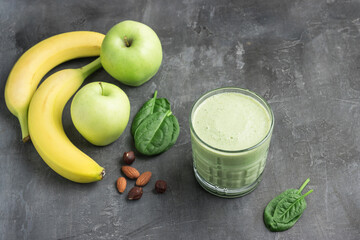 Green detox smoothie in a glass, blended vegetarian drink from spinach leaves, apple, banana fruit and nuts on dark background, healthy eating concept