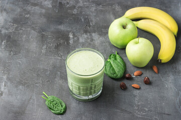 Green detox smoothie in a glass, blended vegetarian drink from spinach leaves, apple, banana fruit and nuts on dark background, healthy eating concept