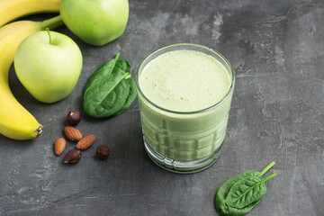 Green detox smoothie in a glass, blended vegetarian drink from spinach leaves, apple, banana fruit and nuts on dark background, healthy eating concept