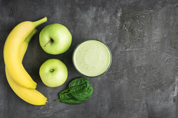 Green detox smoothie in a glass, blended vegetarian drink from spinach leaves, apple and banana fruit on dark background, healthy eating concept, top view