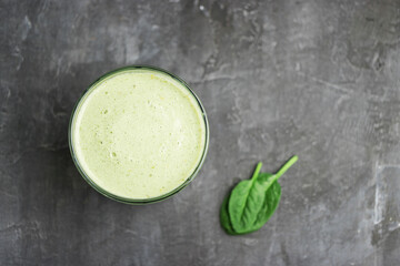 Green detox smoothie in a glass, blended vegetarian drink from spinach leaves on dark background, healthy eating concept, top view