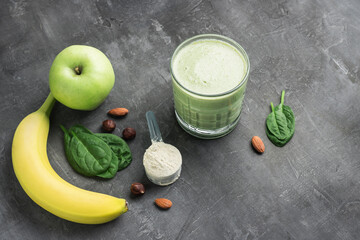 Green detox smoothie in a glass, measuring spoon with protein powder, blended vegetarian drink from...