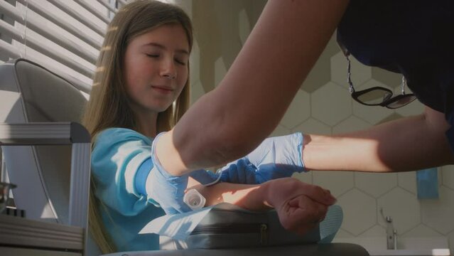 Collecting blood from a girl in a clinic or hospital. A female doctor's hand in rubber gloves inserts a needle into a vein. A blood test at school, a check-up of the body. Donating for patients