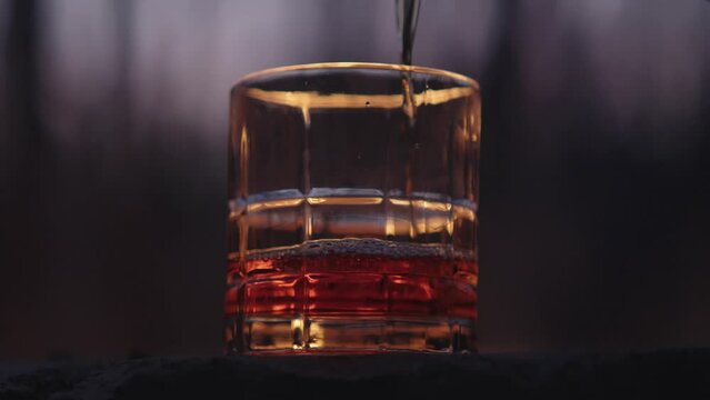 Glass of whiskey being poured in the outdoors in front of a large fire