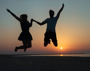 Silhouette of a couple - man and woman jumping on the beach