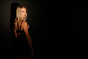 Fototapeta na wymiar Low key portrait of beautiful blonde woman in short black dress