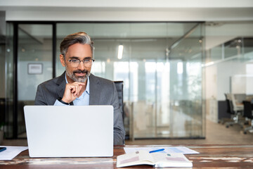 Mature Indian or Latin business man ceo trader using computer, typing, working in modern office,...