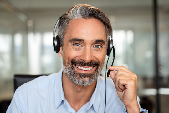 Happy senior latin Hispanic man in wearing headphones, helping as callcenter consult assistant. Smiling mature 40s years old mixed race businessman holding video call with clients partners. Close up