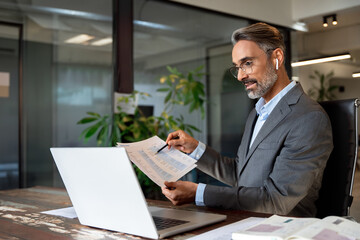 Middle-age Hispanic man using computer remote for business studying, watch online virtual webinar training meeting, video call. Smiling mature Indian or Latin businessman working on laptop in office.