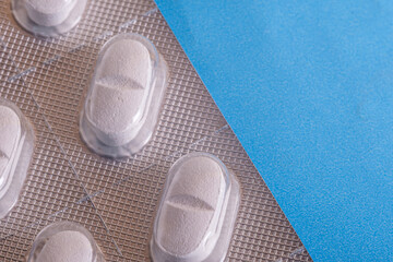 Full frame shot of blister packs. Close-up macro shot of white pills in their packaging on a blue background. Selective focus.