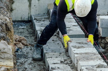 Hard working bricklayer laying concrete blocks on top of concrete foundation ground beam on new...